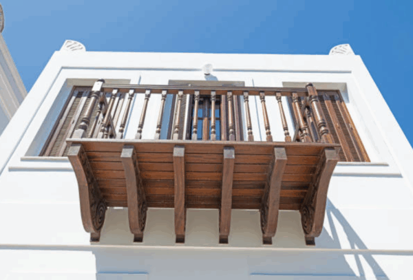 Custom Wooden Balcony Balusters on Outdoor Residential Railing Close-up of custom wooden balcony balusters and railing on a white residential building, showing turned spindle design and wood grain detail.