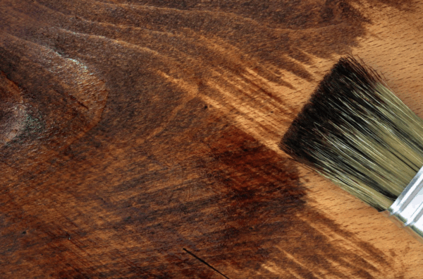 Close-up of wood stain being applied with a brush to highlight grain patterns.