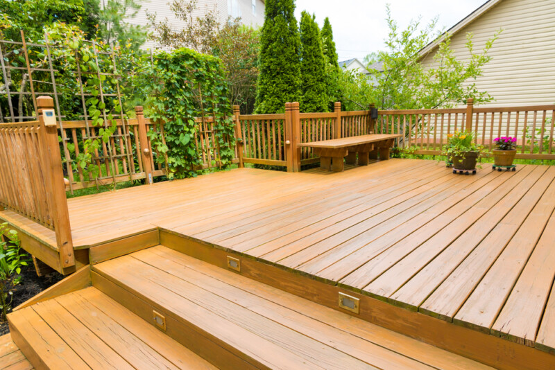 Stained wood deck with matching railing and built-in bench in a backyard.