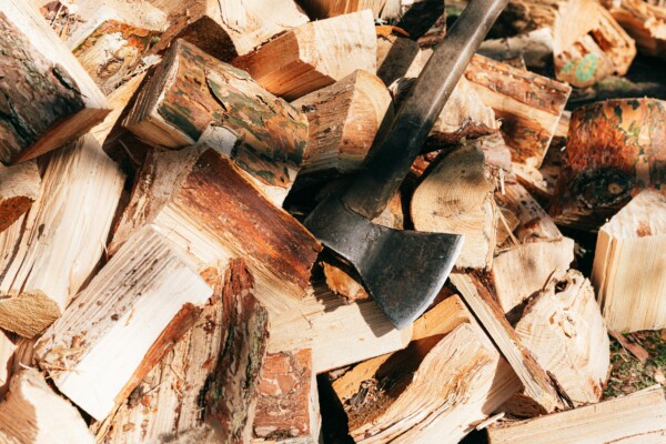 A heavy-duty axe with a wood handle resting in a pile of split firewood.