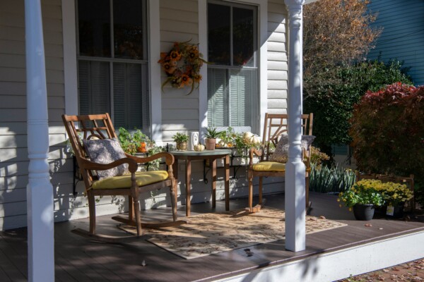 Row of round wood porch columns on a red brick home with wooden rocking chairs at sunset.
