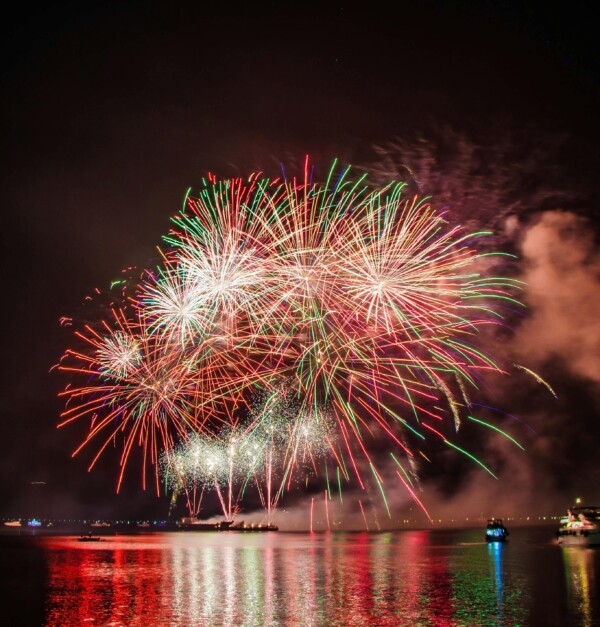 Fireworks Display with Professional Mortar Launch Bright aerial fireworks bursting above water from mortar tubes during a professional display.