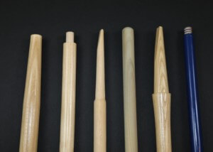 Assorted long wood tool handles stacked in rows, custom-machined for shovels, rakes, brooms, and more.