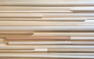 Stack of round wooden dowels in various sizes, wood species, and finishes showing customization options.