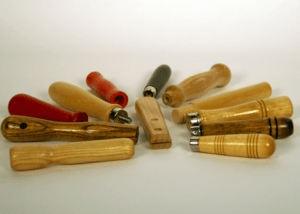 A variety of small wooden tool handles with grooves, beaded grips, and different finishes, custom manufactured for bulk orders.