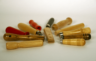 A variety of small wooden tool handles with grooves, beaded grips, and different finishes, custom manufactured for bulk orders.