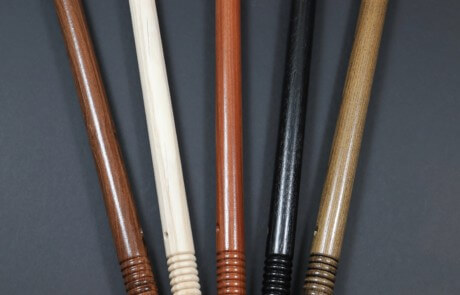 Five wooden police batons with beaded grips in a row, made from finished hardwood.