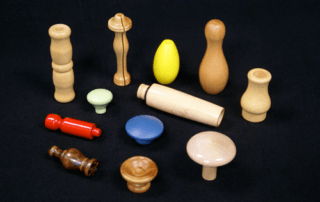 Assorted shaped and turned wood components in different sizes, finishes, and wood species, arranged on a black surface.