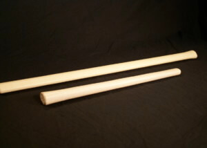 Several custom-shaped hickory wood handles for sledgehammers, axes, and hammers arranged on a work surface.