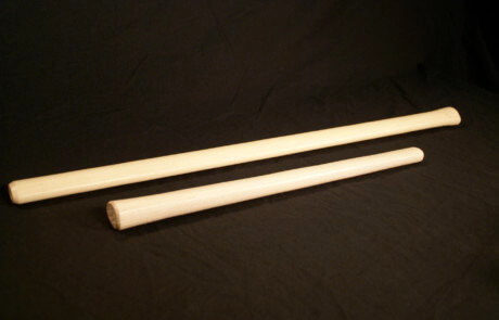 Several custom-shaped hickory wood handles for sledgehammers, axes, and hammers arranged on a work surface.