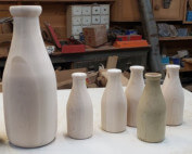 Two custom-turned wooden milk bottles in different sizes designed for promotional or historical display use.