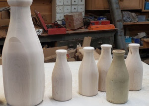 Two custom-turned wooden milk bottles in different sizes designed for promotional or historical display use.