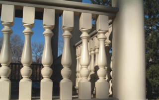 Turned wooden porch balusters lining a white railing on a traditional residential front porch.
