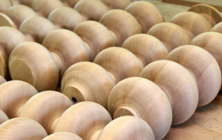 Multiple custom wood turnings laid side by side, showcasing smooth surfaces and varying profiles.