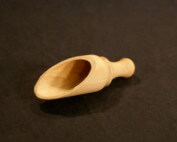A custom wooden scoop featuring turned detailing with slabbing and drilling, displayed on a white surface.