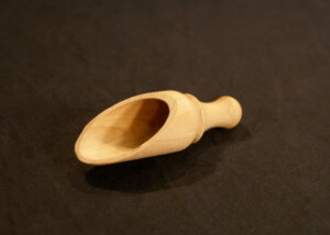 A custom wooden scoop featuring turned detailing with slabbing and drilling, displayed on a white surface.