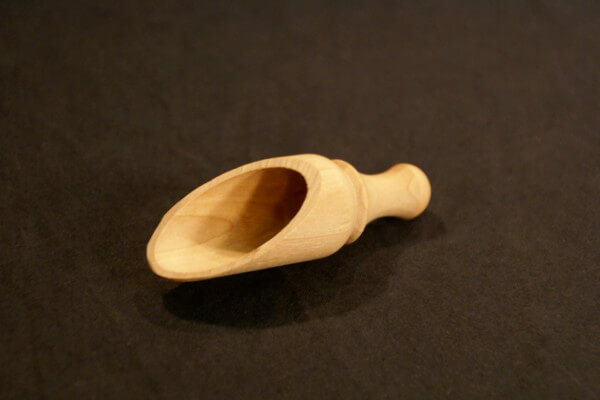 A custom wooden scoop featuring turned detailing with slabbing and drilling, displayed on a white surface.