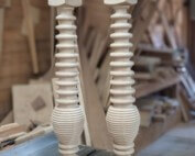 Two custom wood table legs featuring a turned spiral pattern, displayed upright against a workshop background.
