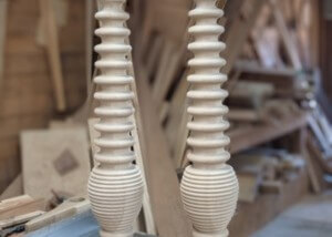 Two custom wood table legs featuring a turned spiral pattern, displayed upright against a workshop background.