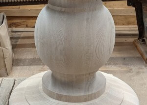 A single custom-turned red oak table base measuring 27 inches in diameter, shown on a workshop floor.