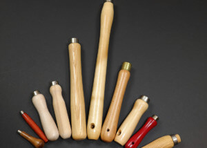 Assorted wood tool handles displayed with custom secondary operations including tenons, holes, tapers, and grooves.