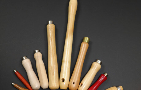 Assorted wood tool handles displayed with custom secondary operations including tenons, holes, tapers, and grooves.