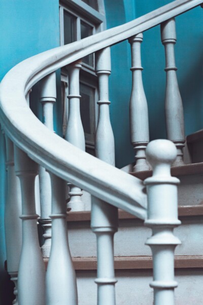 Close-up of white painted turned wood balusters and curved handrail on a historic staircase, showing the profile detail relevant to custom baluster matching and replacement.